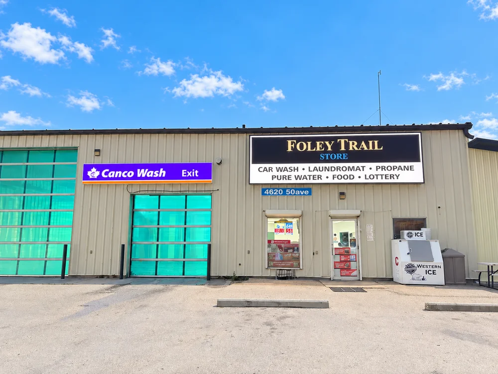 Foley Trail store entrance and green car wash doors beneath a blue sky